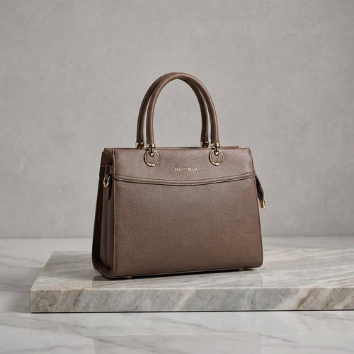 A structured brown leather handbag with double top handles and gold-tone hardware, displayed on a marble slab against a textured gray background.