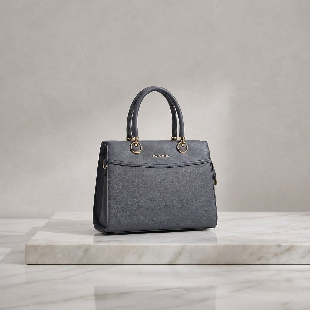 A structured gray leather handbag with double top handles and gold-tone hardware, displayed on a white marble slab against a neutral gray studio background.