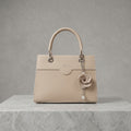A structured beige leather handbag with silver-tone hardware, featuring a top handle, a decorative flower charm with a pearl drop, and the brand name 'V. SEAL.