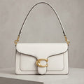 A structured white leather shoulder bag with a gold-tone C-shaped hardware clasp and a thin black-and-white strap, displayed on a light gray pedestal against a textured gray background.