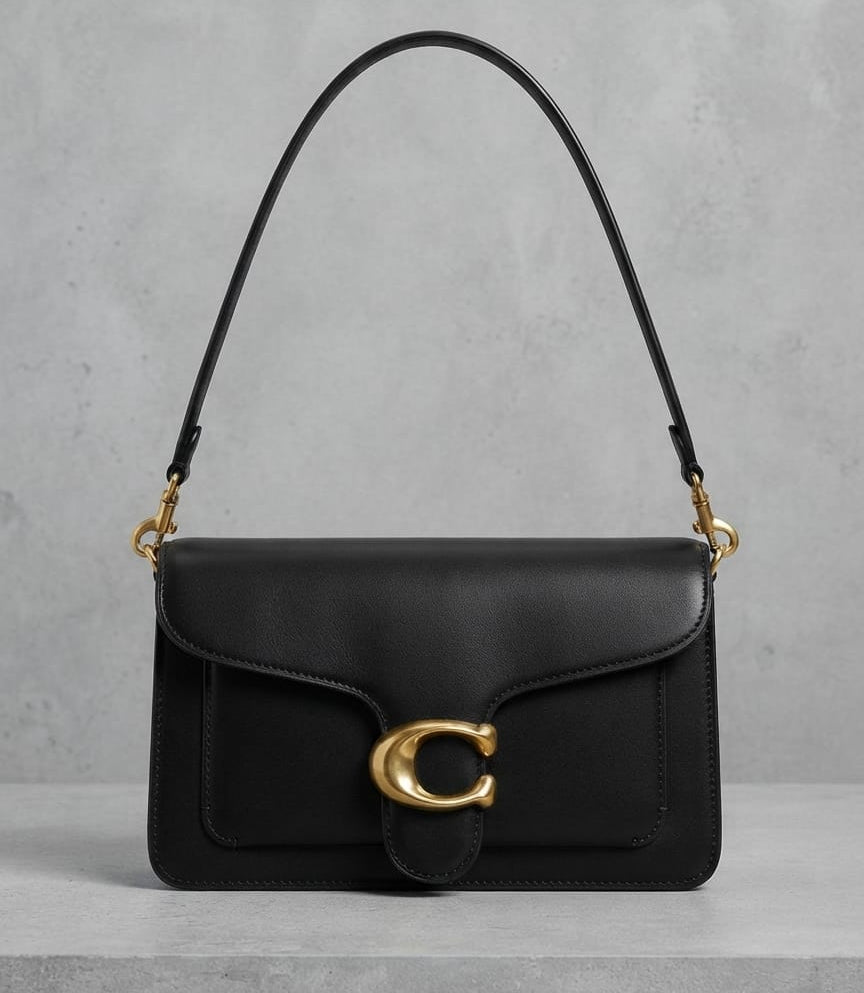 A black leather shoulder bag with a gold-tone C logo clasp and a thin black shoulder strap, displayed on a light gray textured surface.