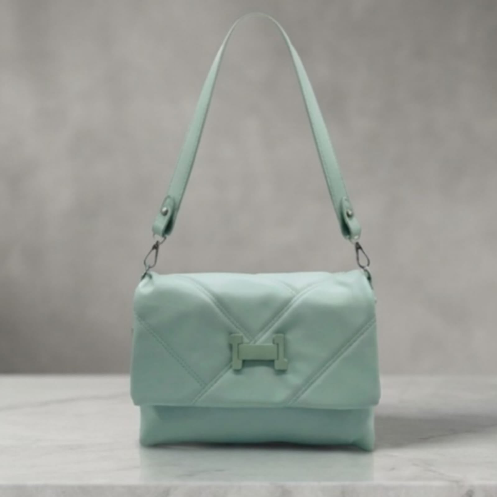 A mint green quilted leather shoulder bag with a prominent H-shaped turn-lock closure on the front flap, resting on a light marble surface against a textured gray background.